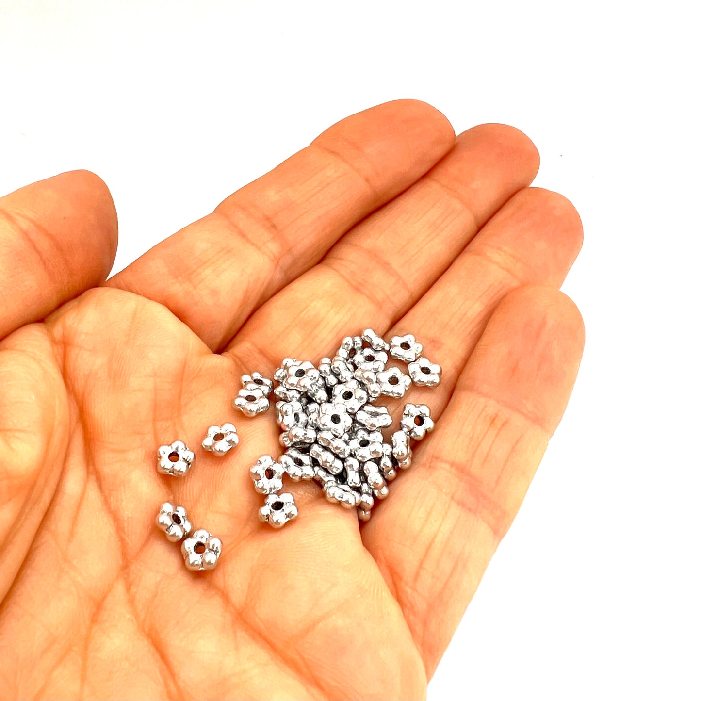 Hand holding small silver flower beads on a white background