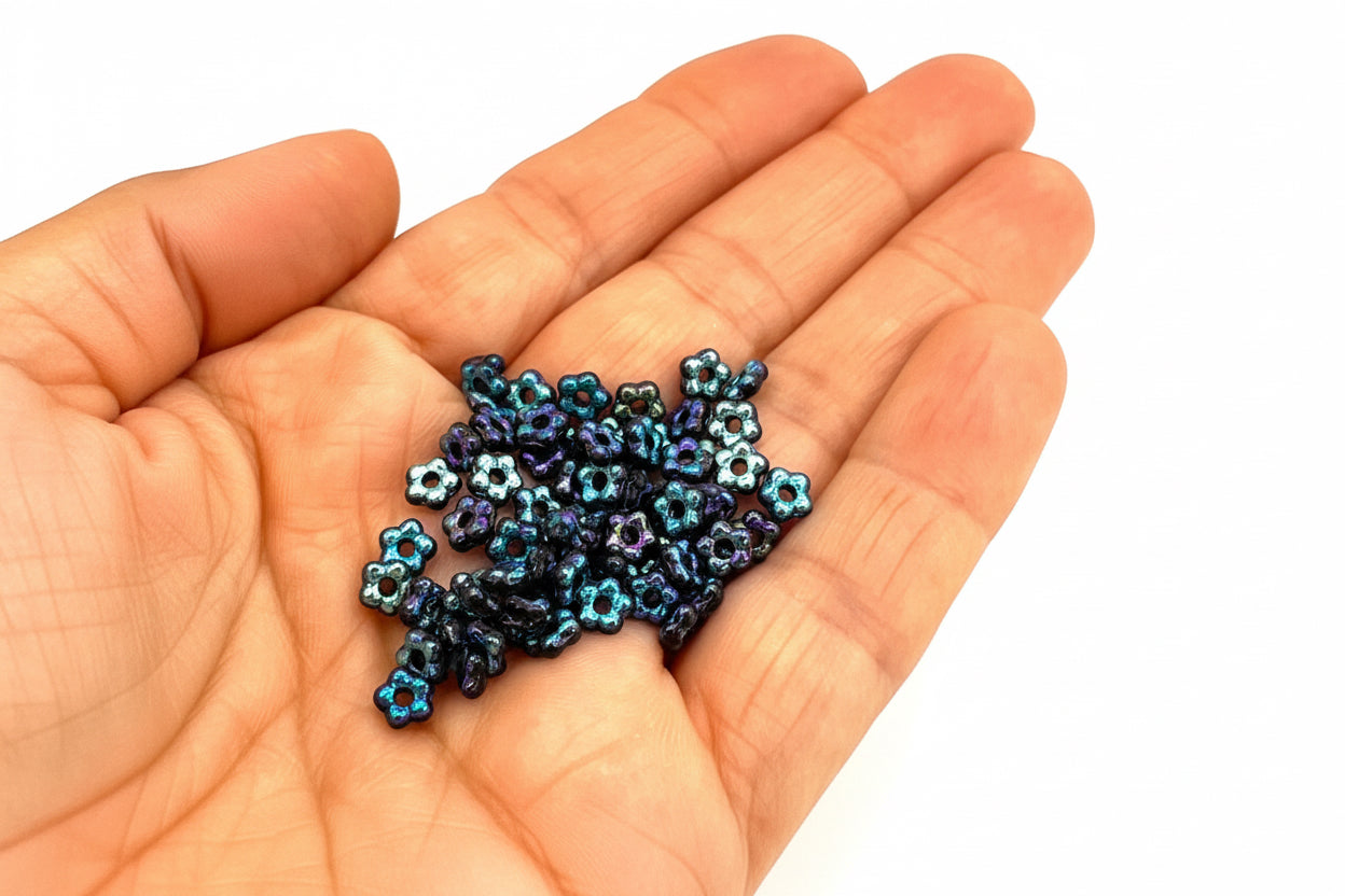 Hand holding small metallic flower-shaped beads on a white background