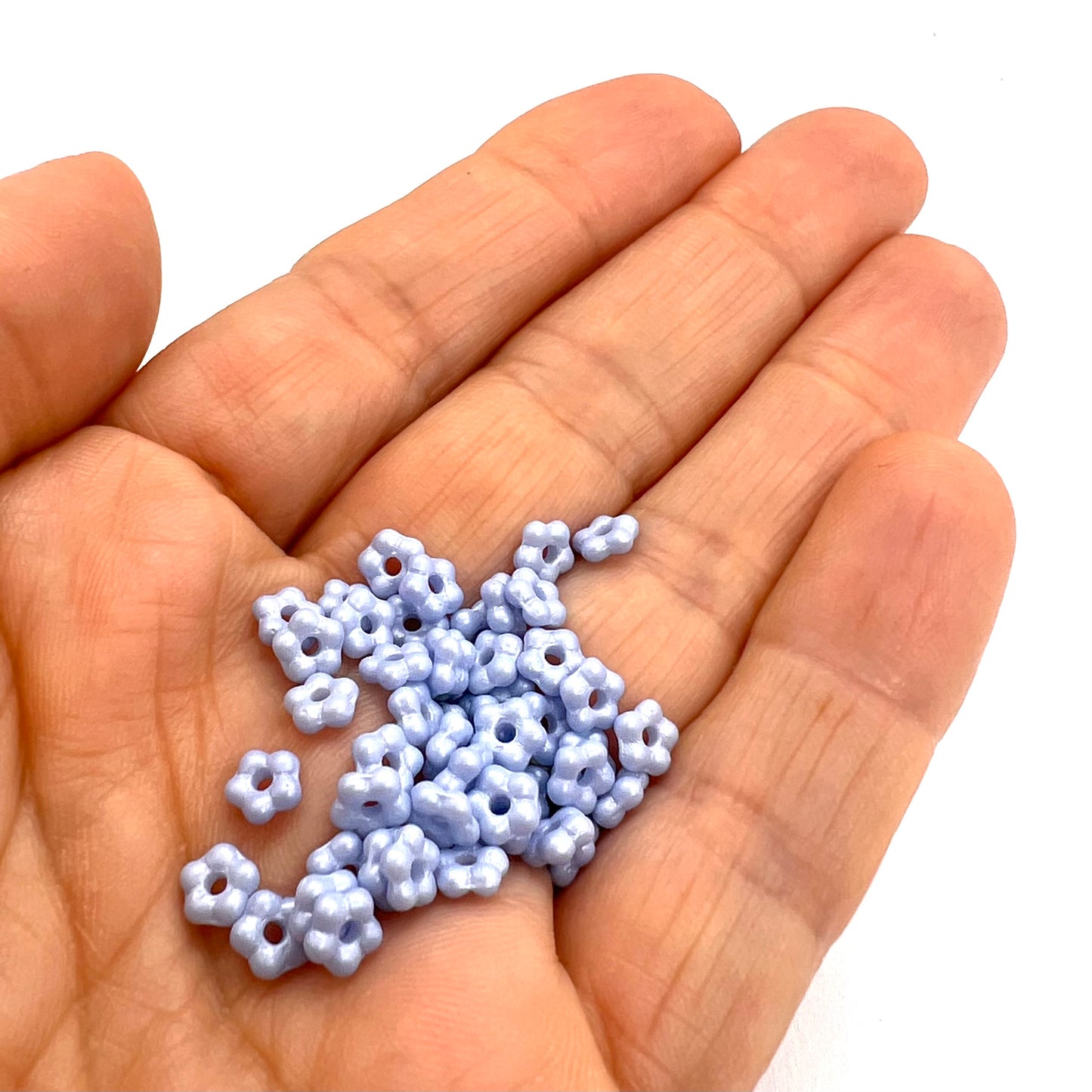 Hand holding small blue flower beads on a white background